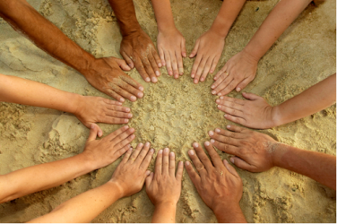 Children and adults shape a circle with their hands on sand